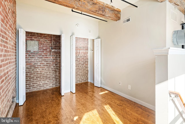 unfurnished bedroom with brick wall, wood finished floors, beam ceiling, and baseboards