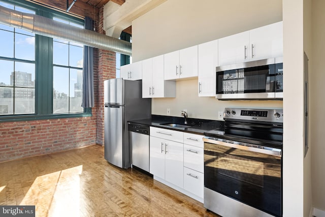 kitchen featuring brick wall, stainless steel appliances, a sink, light wood-style floors, and white cabinets