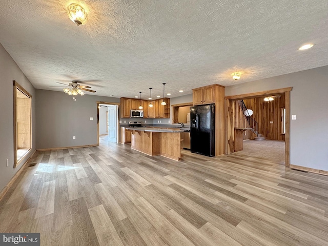 kitchen with decorative light fixtures, a center island, a textured ceiling, light wood-type flooring, and stainless steel appliances