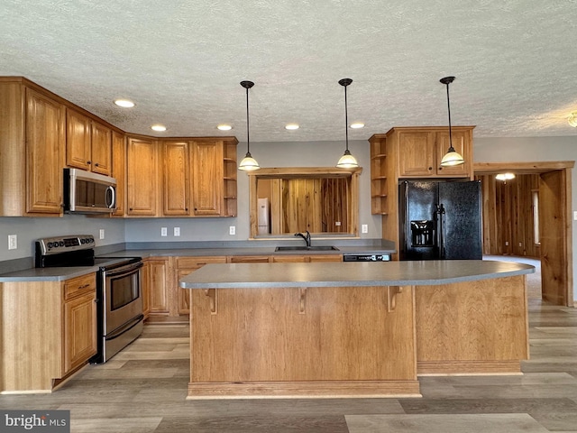 kitchen with sink, light hardwood / wood-style flooring, appliances with stainless steel finishes, a kitchen island, and decorative light fixtures