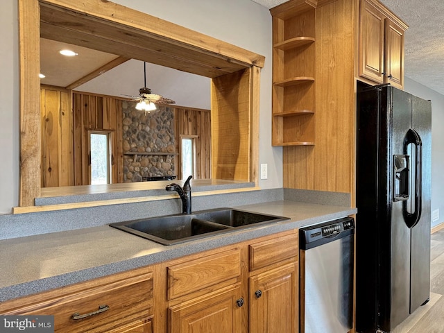 kitchen with sink, ceiling fan, black fridge, a stone fireplace, and stainless steel dishwasher