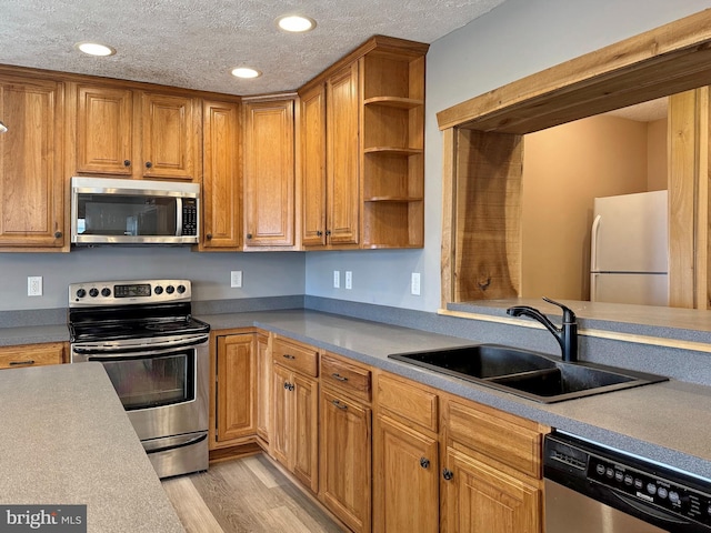 kitchen featuring sink, light hardwood / wood-style flooring, a textured ceiling, and appliances with stainless steel finishes