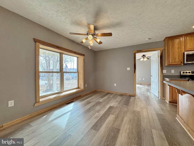 kitchen featuring ceiling fan, appliances with stainless steel finishes, a textured ceiling, and light wood-type flooring