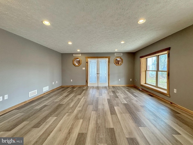 unfurnished living room featuring a textured ceiling, light hardwood / wood-style floors, and french doors