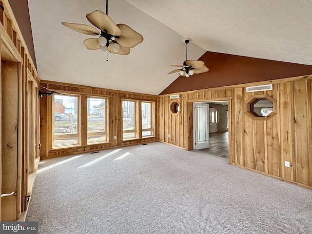 unfurnished living room with vaulted ceiling, wood walls, light colored carpet, ceiling fan, and a textured ceiling