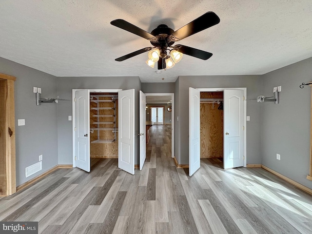 unfurnished bedroom featuring multiple closets, ceiling fan, light hardwood / wood-style flooring, and a textured ceiling