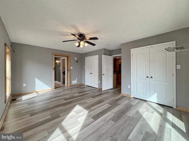 unfurnished bedroom with ceiling fan, light wood-type flooring, a textured ceiling, and two closets