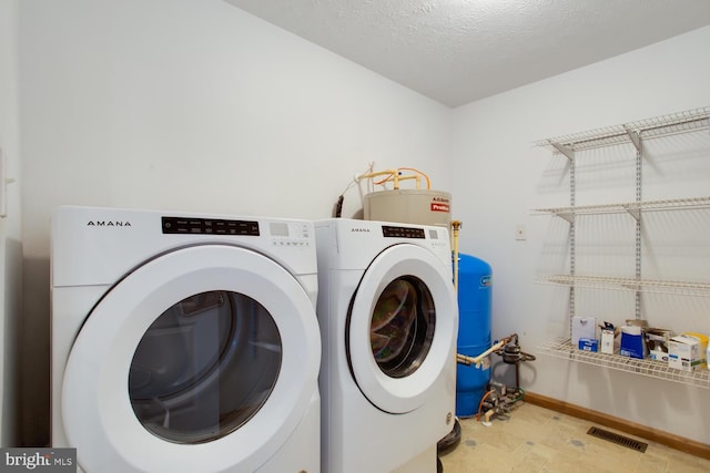 washroom with water heater, separate washer and dryer, and a textured ceiling