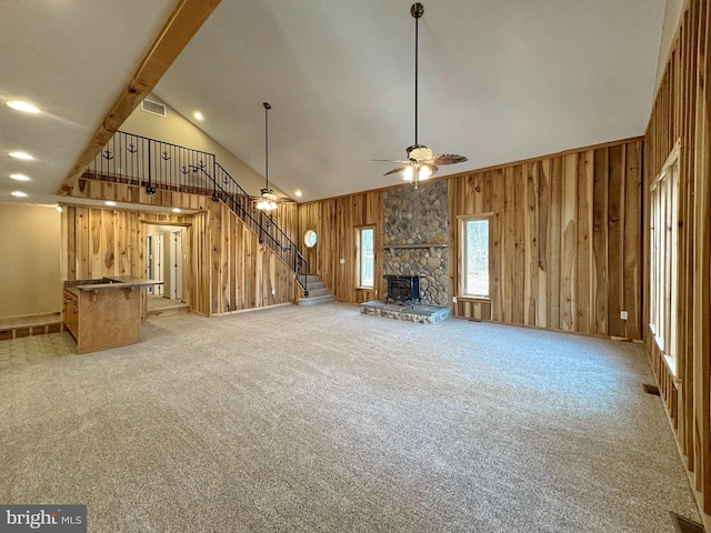 unfurnished living room featuring ceiling fan, wooden walls, high vaulted ceiling, light carpet, and a stone fireplace