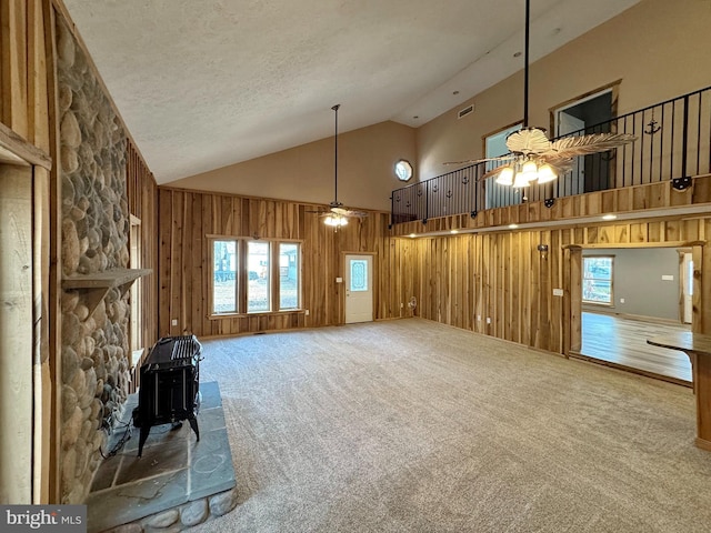 unfurnished living room with ceiling fan, high vaulted ceiling, carpet, a textured ceiling, and wood walls