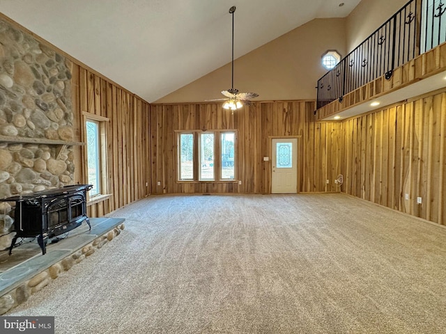 unfurnished living room with ceiling fan, carpet floors, a wood stove, and wood walls