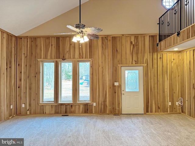 unfurnished living room with ceiling fan, carpet flooring, high vaulted ceiling, and wood walls