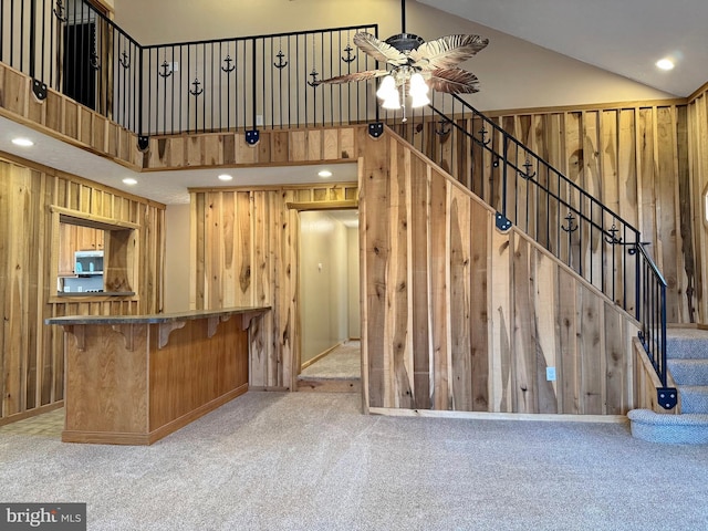 kitchen featuring a kitchen bar, wood walls, light colored carpet, high vaulted ceiling, and ceiling fan