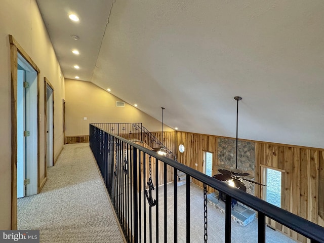 hallway featuring lofted ceiling, light colored carpet, and wood walls