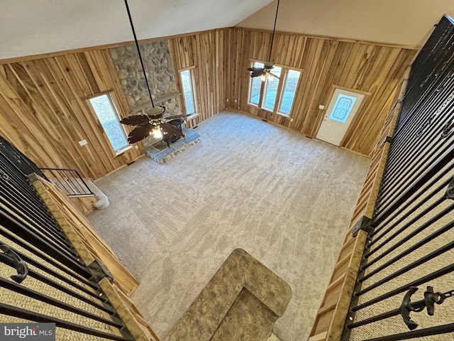 unfurnished living room featuring ceiling fan, carpet, high vaulted ceiling, and wooden walls