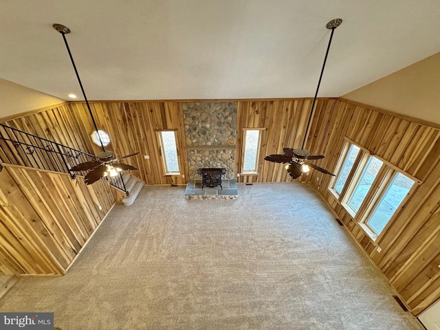 unfurnished living room with ceiling fan, wooden walls, and carpet