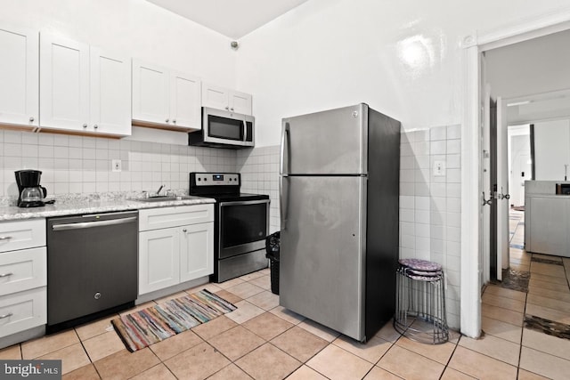 kitchen with washer / clothes dryer, white cabinetry, light tile patterned floors, stainless steel appliances, and light stone countertops