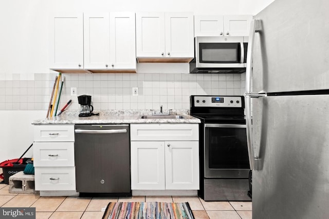 kitchen with sink, light tile patterned floors, stainless steel appliances, light stone countertops, and white cabinets