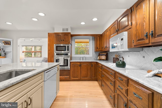 kitchen featuring appliances with stainless steel finishes, light stone countertops, light hardwood / wood-style floors, and a wealth of natural light