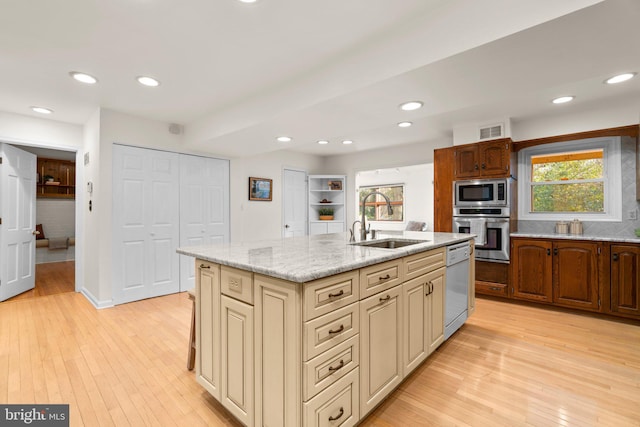 kitchen with appliances with stainless steel finishes, a kitchen island with sink, sink, and light hardwood / wood-style flooring