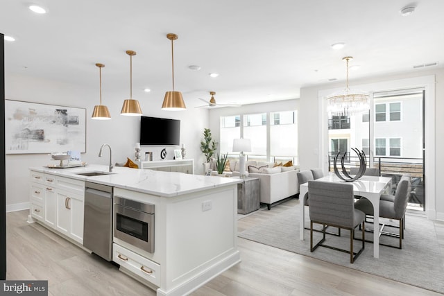 kitchen with sink, hanging light fixtures, white cabinets, and a center island with sink