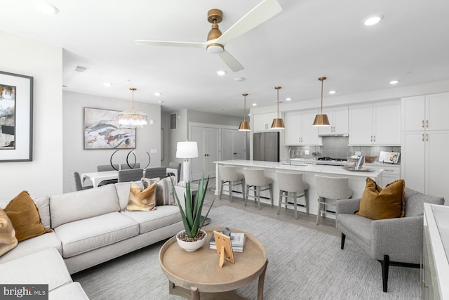 living room with sink, ceiling fan with notable chandelier, and light wood-type flooring