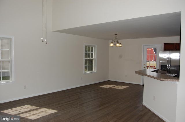 unfurnished dining area with dark wood-style flooring, an inviting chandelier, and baseboards