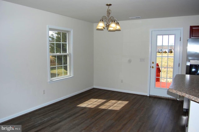 unfurnished dining area with dark wood-style flooring, plenty of natural light, baseboards, and an inviting chandelier