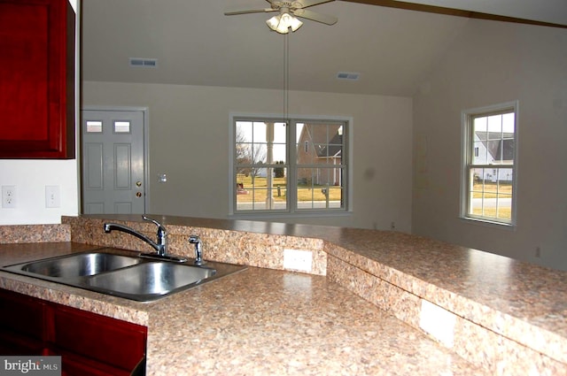 kitchen featuring reddish brown cabinets, visible vents, vaulted ceiling, and a sink