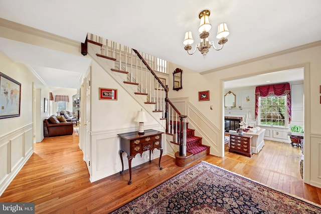 foyer entrance with light wood-type flooring, crown molding, and a notable chandelier