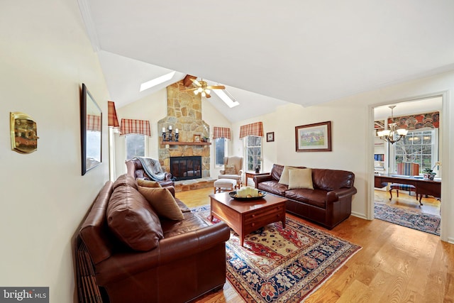 living room with a fireplace, light hardwood / wood-style floors, lofted ceiling with skylight, and ceiling fan with notable chandelier