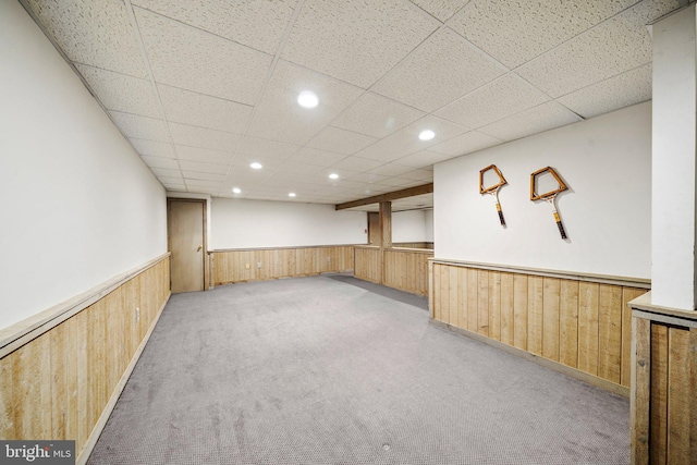 carpeted spare room with wooden walls and a drop ceiling