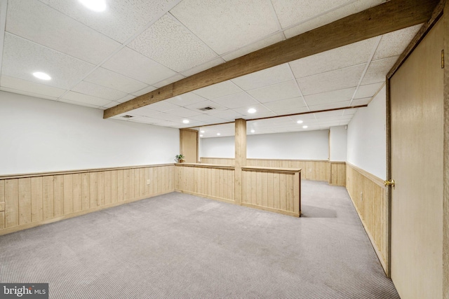 basement featuring a paneled ceiling, light carpet, and wooden walls