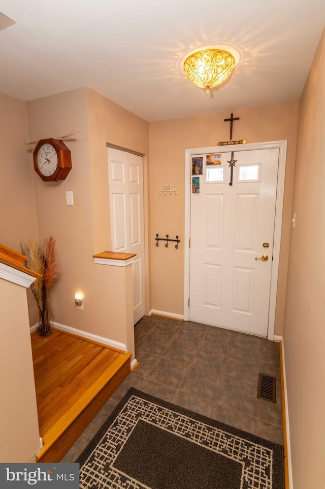 foyer entrance with dark tile patterned floors, visible vents, and baseboards