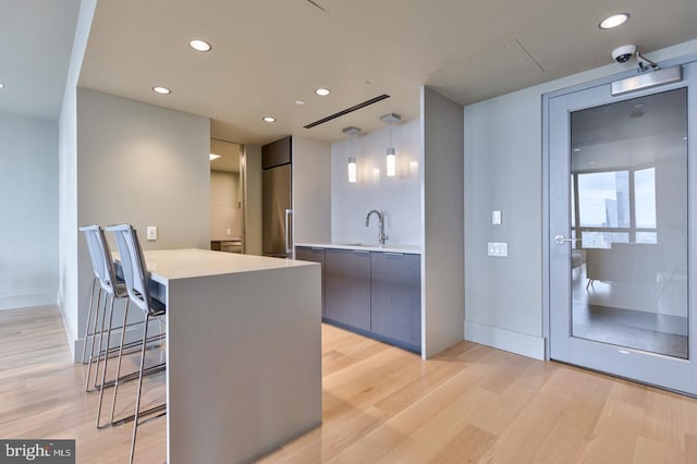 kitchen with hanging light fixtures, light hardwood / wood-style flooring, sink, and a kitchen bar