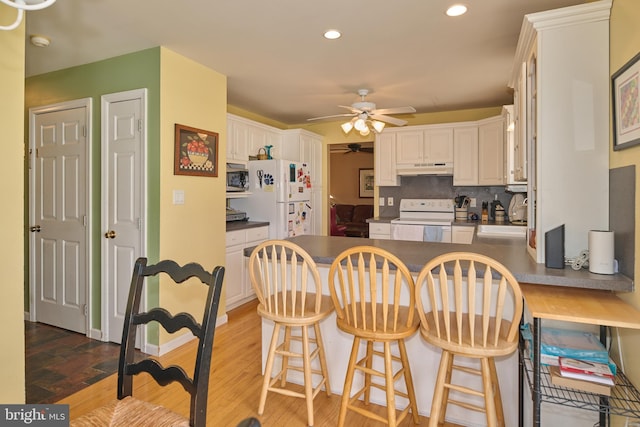 kitchen with sink, kitchen peninsula, hardwood / wood-style flooring, white appliances, and decorative backsplash