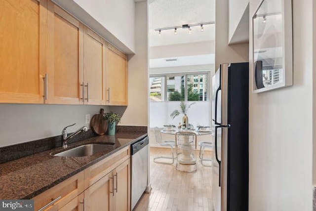 kitchen with sink, fridge, light brown cabinetry, stainless steel dishwasher, and dark stone counters