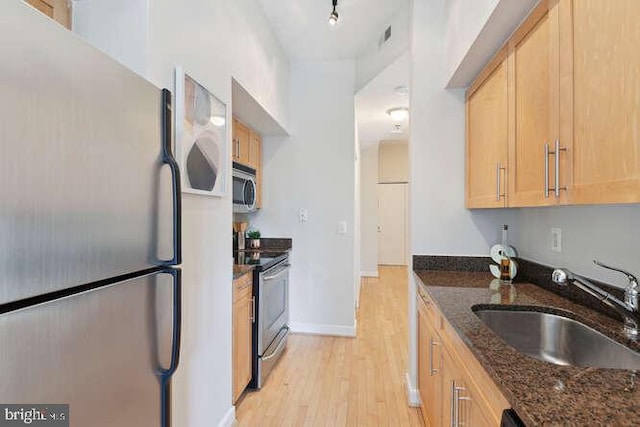 kitchen with sink, light hardwood / wood-style flooring, light brown cabinets, dark stone counters, and stainless steel appliances