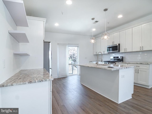 kitchen with white cabinets, hanging light fixtures, a kitchen island with sink, light stone counters, and stainless steel appliances