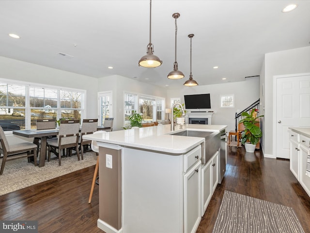 kitchen with pendant lighting, white cabinetry, dark hardwood / wood-style floors, and a center island with sink