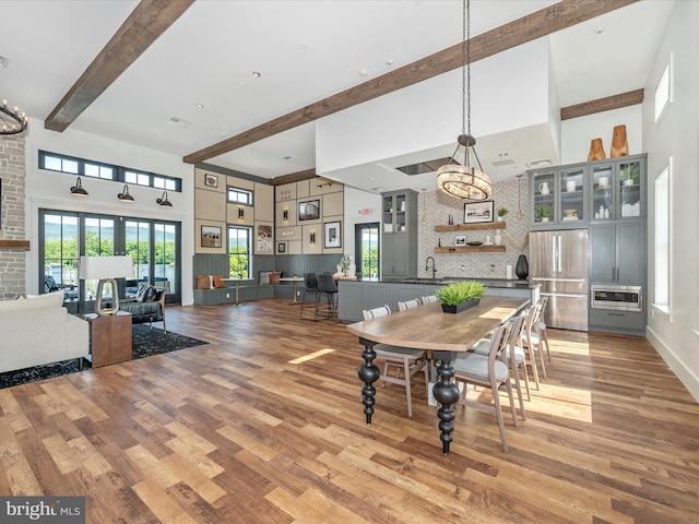 dining space with a towering ceiling, heating unit, wood-type flooring, sink, and beam ceiling