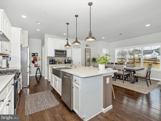 kitchen with pendant lighting, sink, appliances with stainless steel finishes, white cabinetry, and a center island with sink