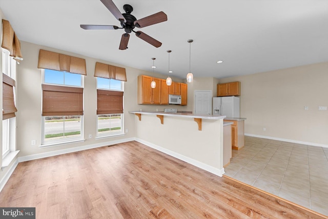 kitchen with pendant lighting, white appliances, a kitchen breakfast bar, light hardwood / wood-style floors, and kitchen peninsula