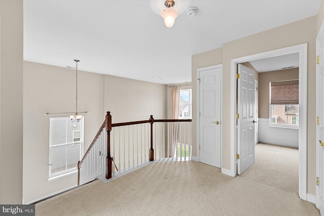 hall featuring light carpet and an inviting chandelier