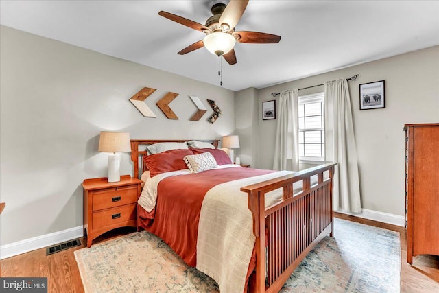 bedroom featuring ceiling fan, wood finished floors, visible vents, and baseboards