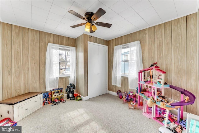 rec room with carpet, wooden walls, ceiling fan, and a wealth of natural light