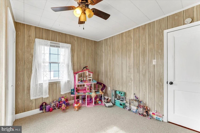 rec room with carpet, wooden walls, ceiling fan, and crown molding