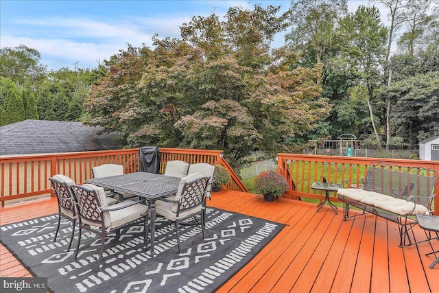 deck featuring outdoor dining area, a playground, and fence