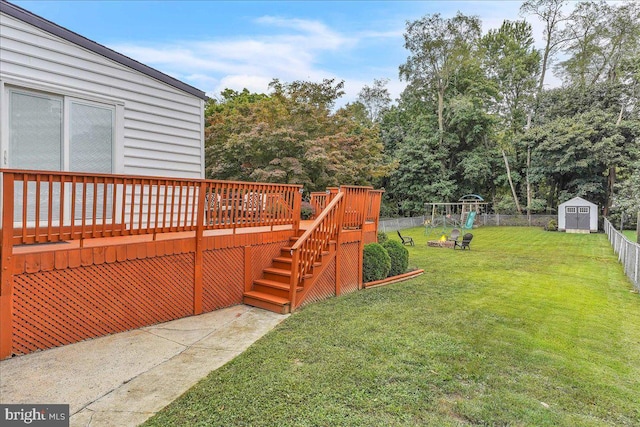 view of yard featuring a deck, a playground, a fenced backyard, an outdoor structure, and a storage unit