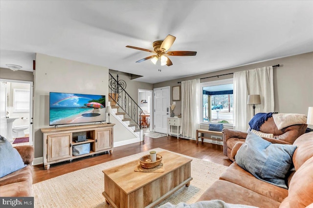 living room featuring a ceiling fan, stairway, baseboards, and wood finished floors